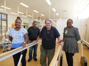 Scott Siota and two other healthcare professionals stand beside a patient using parallel bars for rehabilitation therapy.
